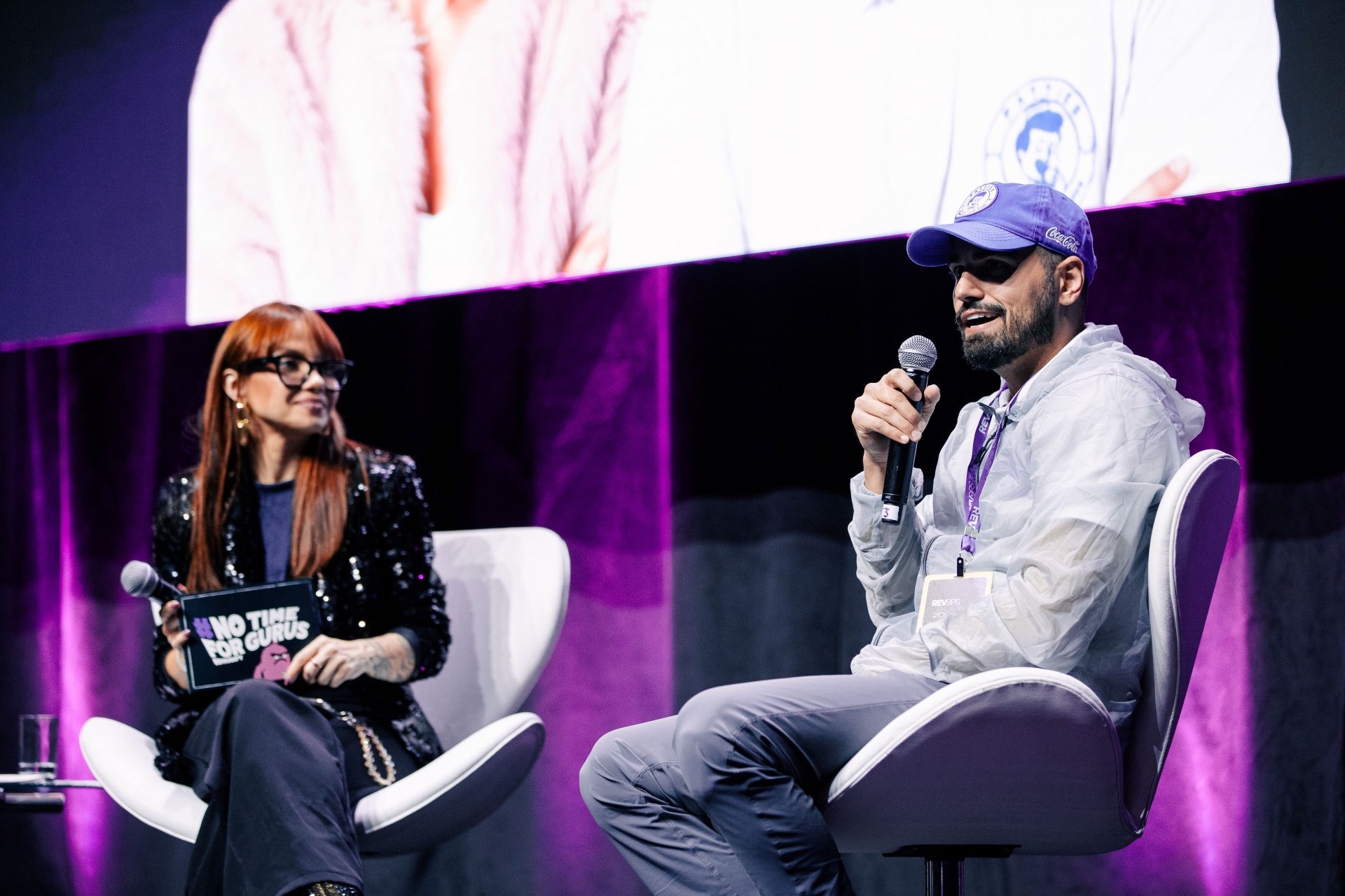 Henrique Azeredo fala ao microfone durante o painel, acompanhado pela mediadora Carol Lima.